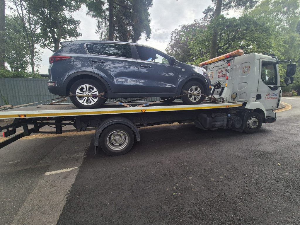 Car recovery truck transporting an SUV on a flatbed roadside in the West Midlands